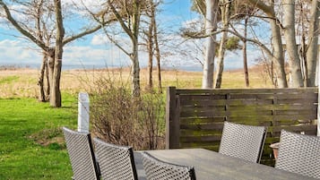 An outdoor seating area with a table and chairs, surrounded by trees and a grassy field.