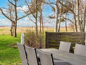 Un espace extérieur aménagé avec une table et des chaises, entouré d’arbres et d’un champ d’herbe.