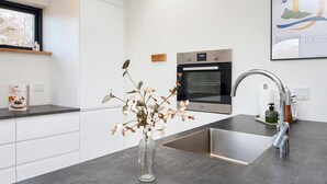 Una cocina moderna con horno empotrado, pileta de acero inoxidable y un florero con flores secas en la encimera.