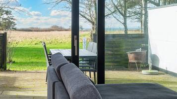 Ein moderner Außenbereich mit Sitzgelegenheit und Blick auf ein Wiesenfeld und Bäume.