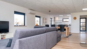 Una sala de estar moderna con un sofá seccional gris, un televisor de pantalla plana y un comedor con una mesa y sillas de madera.