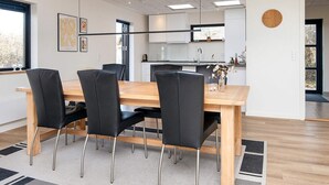Un comedor moderno con una mesa de madera y sillas negras, una cocina al fondo y un reloj en la pared.