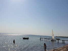 A beach with a sailboat, a dock, and a person standing in the water.