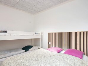 A bunk bed with a lower bunk and a top bunk, a headboard with vertical slats, and a bed with a floral-patterned blanket and pillows.