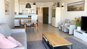 A modern living room with a sofa, a coffee table, and a TV. There is a dining area with a table and chairs. The kitchen is visible in the background. - Apartment in Nieuwpoort Near the Beach (Nieuwpoort)
