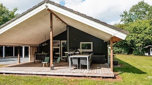 A covered outdoor patio with a dining table and chairs, a grill, and a TV mounted on the wall. - 4 Person Holiday Home in Oksbol (Oksbol)