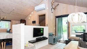 A modern cabin interior with a TV, wooden walls, a fireplace, and a dining area. - 4 Person Holiday Home in Oksbol (Oksbol)