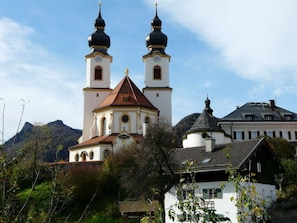 Una iglesia con dos torres y un campanario, rodeada de árboles y una montaña al fondo.