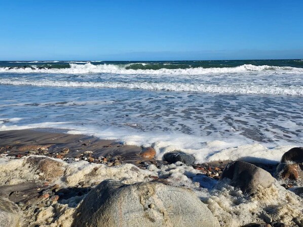 A rocky beach with waves, clear sky, and distant horizon.