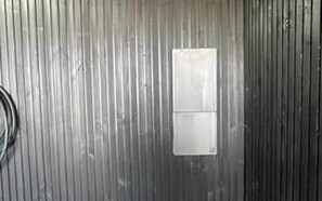 A metallic wall with a rectangular object, possibly a vent or panel, and a coiled cable.
