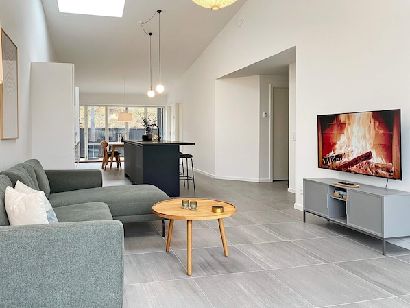 A modern living room with a grey sofa, a wooden coffee table, and a flat-screen TV displaying a fireplace.