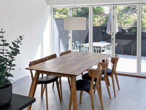 A modern dining area with a wooden table and chairs, a potted plant, and a view of the outdoor patio.