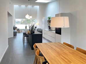 A modern kitchen with a central island, bar stools, a dining table with chairs, and pendant lighting. - 4 Person Holiday Home in Gilleleje (Gilleleje)