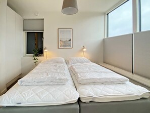 A twin room with two beds, a window, a picture on the wall, and a plant.