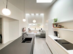 A modern kitchen with a central island, pendant lighting, and a view to a living area with a sofa and coffee table.