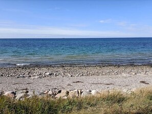 A pebbly beach with clear blue water and a distant horizon.