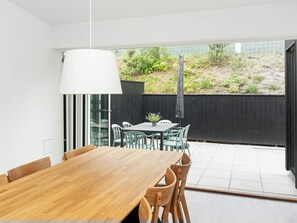 A modern dining area with a wooden table and chairs, a hanging light fixture, and a view of a garden through a glass door. - 4 Person Holiday Home in Gilleleje (Gilleleje)