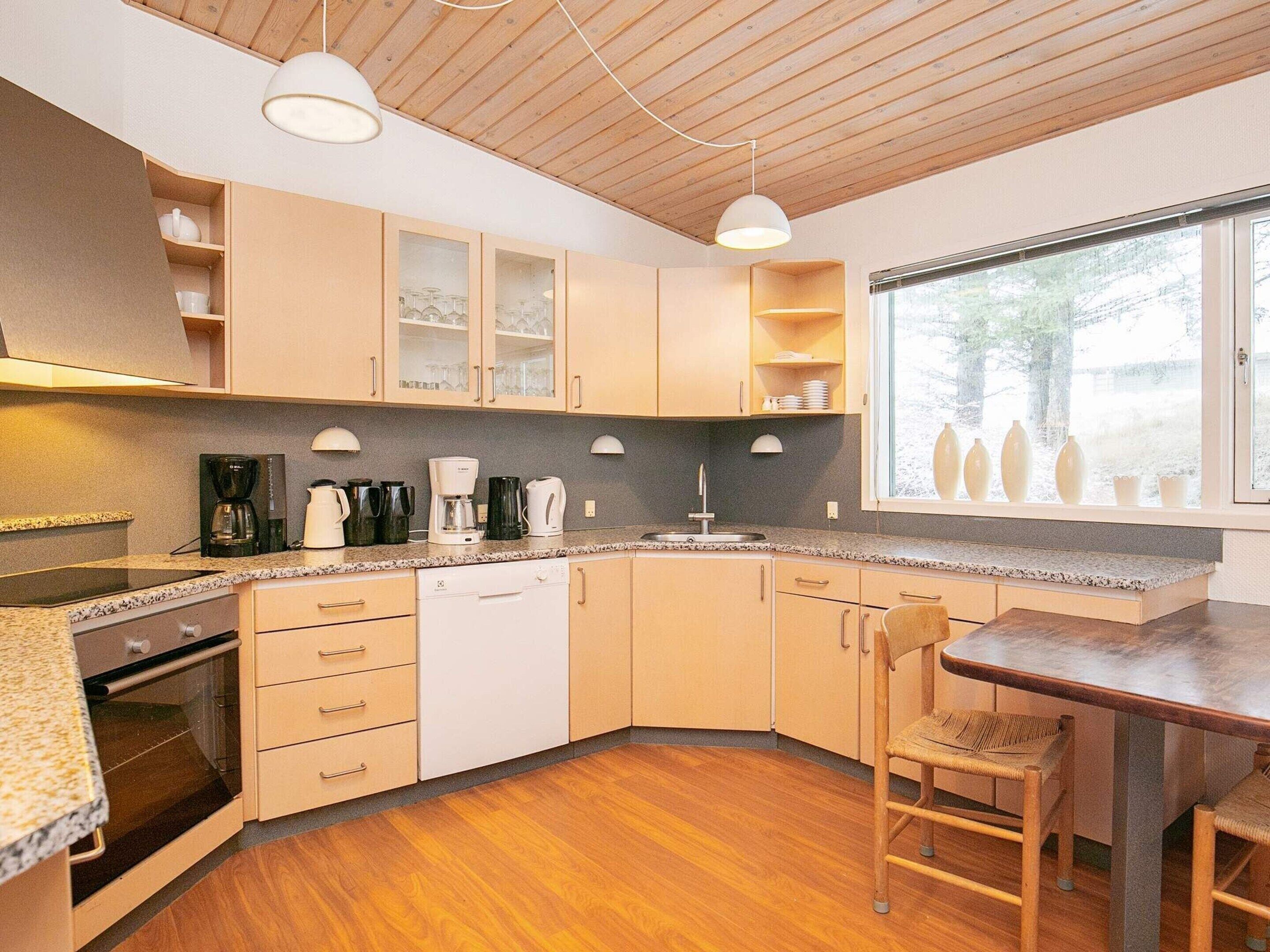 Cocina compacta con armarios de madera, horno integrado y comedor con mesa y sillas de madera.