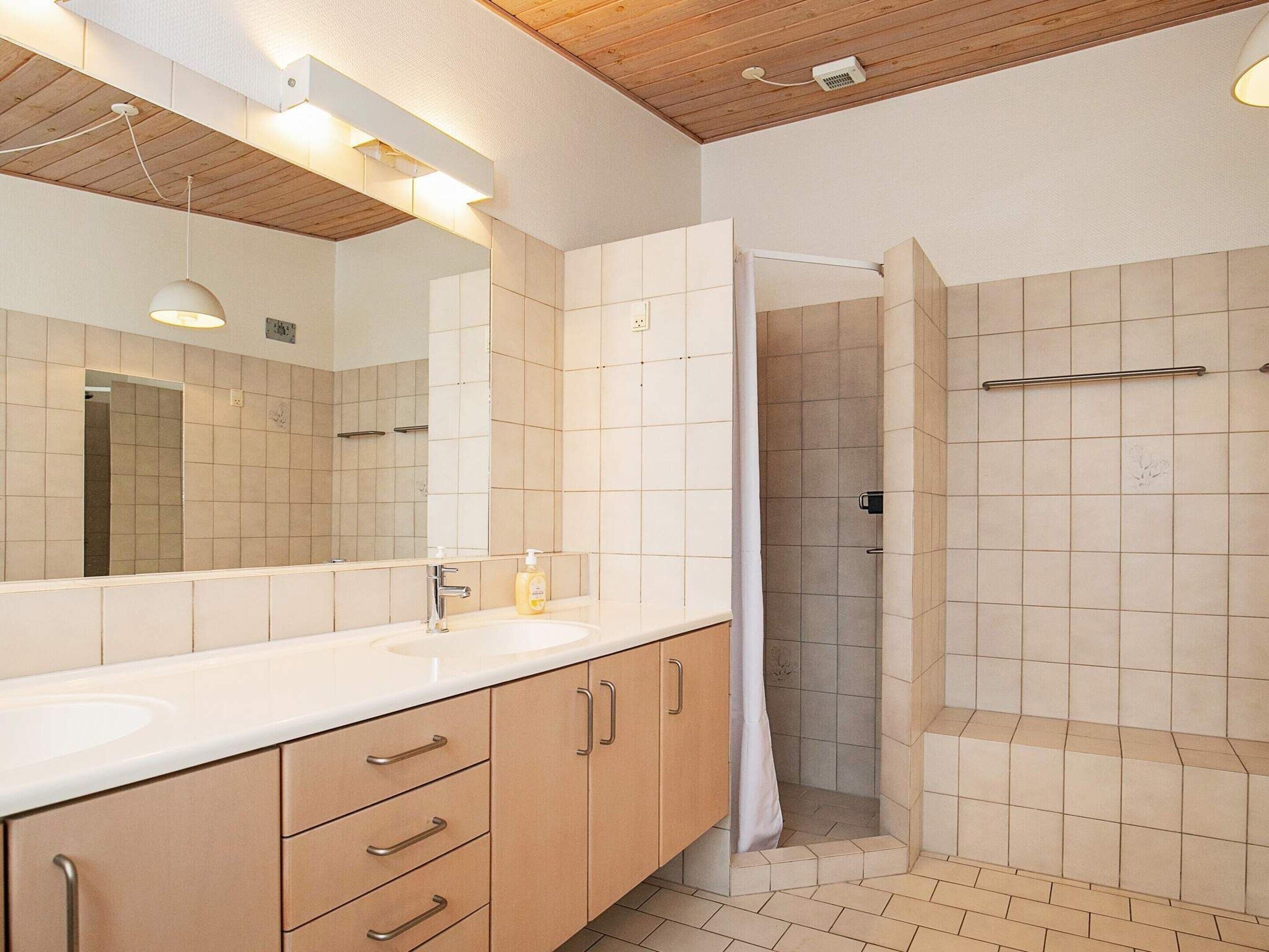 A modern bathroom with a large mirror, a sink, and a shower area.