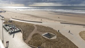 Ein Strand mit Promenadenweg, Aussichtsplattform und einem stürmischen Himmel.