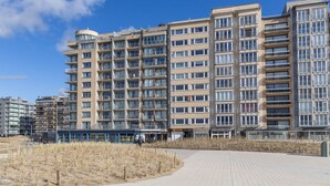 Ein modernes Mehrfamilienhaus mit Balkonen, einem gepflasterten Weg und blauem Himmel.