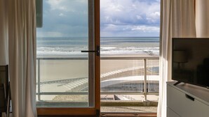 Ein Zimmer mit großem Fenster mit Blick auf den Strand und den Ozean, einem Fernseher und einer Aussicht auf ein Stadion.