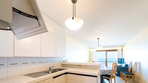 Eine moderne Küche mit Geschirrspüler, Spüle und Herd. Ein Essbereich mit Tisch und Stühlen bietet Blick auf das Meer durch große Fenster.