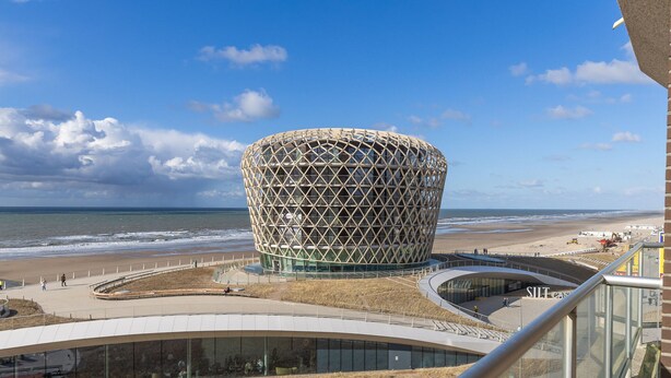 Ein modernes Gebäude mit einem einzigartigen geometrischen Design, nahe einem Strand unter wolkenlosem Himmel.