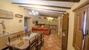 A dining area with a wooden table and chairs, a fireplace, and a cozy seating area with an orange sofa. - Holiday Home in Laroya With Mountain Views (Laroya)