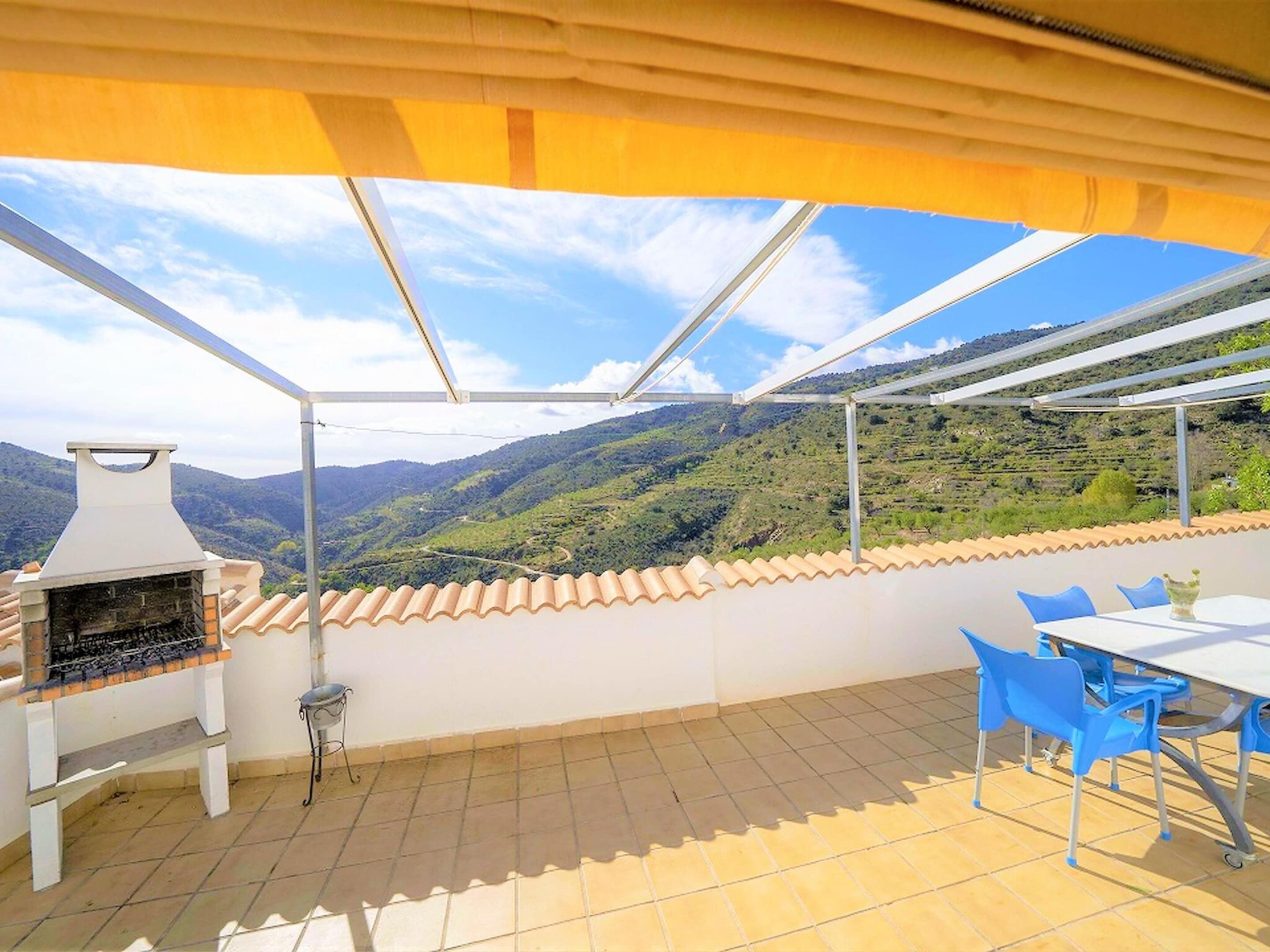 An outdoor patio with a barbecue grill, a table with chairs, and a view of a hilly landscape.