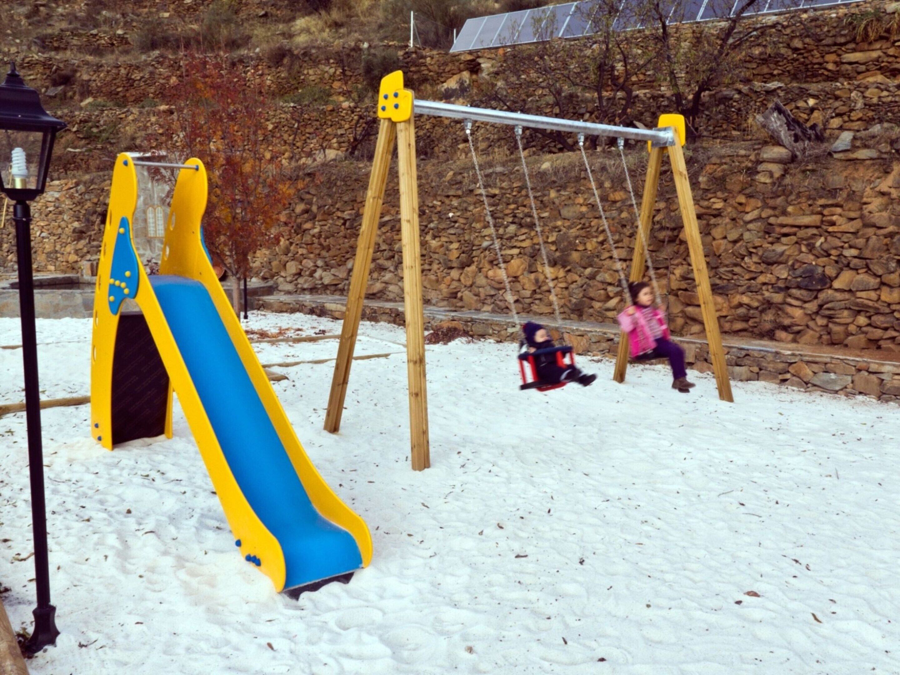 A playground with a slide and swings in a snowy setting.