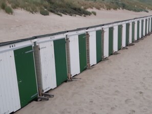Eine Reihe von Strandhäusern mit den Nummern 448 bis 461, die an einem Sandstrand aufgereiht sind.