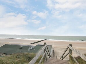A beach with a wooden walkway leading to a building with a green roof. - De Zon in Zeeland Holiday Residence (Vlissingen)