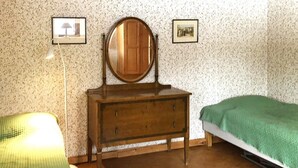 A bedroom with a wooden dresser, a bed with a green blanket, a lamp, and two framed pictures on the wall.