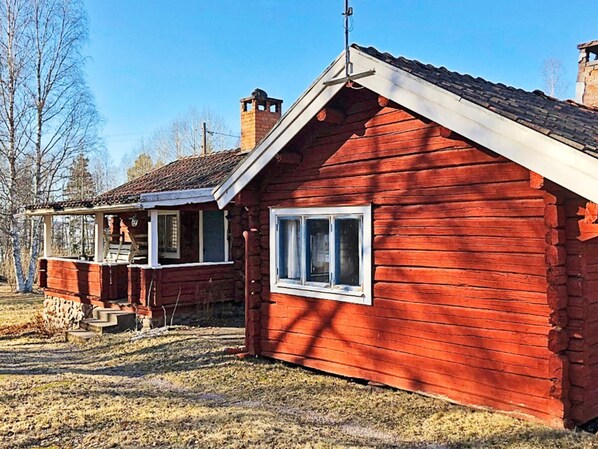 A red wooden cabin with a porch and a chimney.
