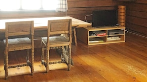A wooden dining table with chairs, a television on a stand, and a window with curtains.