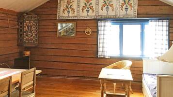 A wooden cabin interior with a dining table, chairs, a window with curtains, and a wall-mounted decorative panel.