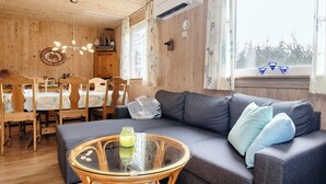 A cozy room with a sofa, a glass coffee table, and a dining area with wooden chairs and a table. - 5 Person Holiday Home in Asaa (Asaa)