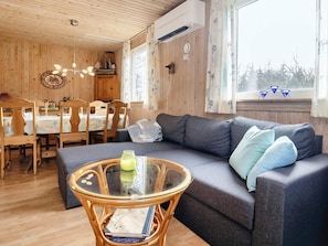 Una habitación acogedora con sofá, una mesa de centro de vidrio y un comedor con sillas y mesa de madera.