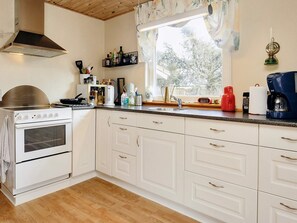 Una cocina con armarios blancos, una estufa, una ventana con cortinas y varios utensilios de cocina sobre la encimera.