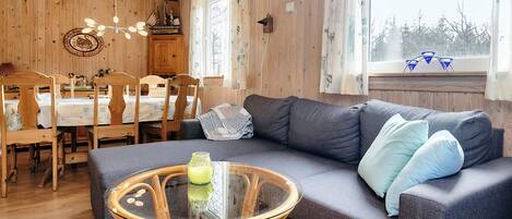 A cozy room with a sofa, a glass coffee table, and a dining area with wooden chairs and a table.