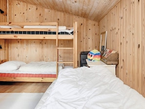Habitación con literas de madera, una escalera, un escritorio con espejo y un peluche colorido.