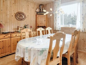 Una habitación con paneles de madera, una mesa redonda para comer, sillas, un armario y una ventana con cortinas.
