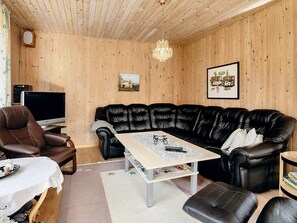 Una sala de estar con un sofá de cuero negro, un sillón de cuero marrón, techo de madera, candelabro y un cuadro enmarcado en la pared.