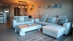Una sala de estar moderna con un sofá modular, una mesa de centro y una cocina al fondo.