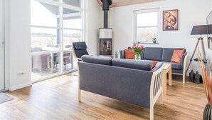 A spacious living room with a large window, a fireplace, a grey sofa, and a wooden floor. - 6 Person Holiday Home in Tarm (Hemmet)