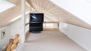 A high-ceilinged attic room with a television on a stand, wooden beams, and a view through the skylight. - 6 Person Holiday Home in Tarm (Hemmet)