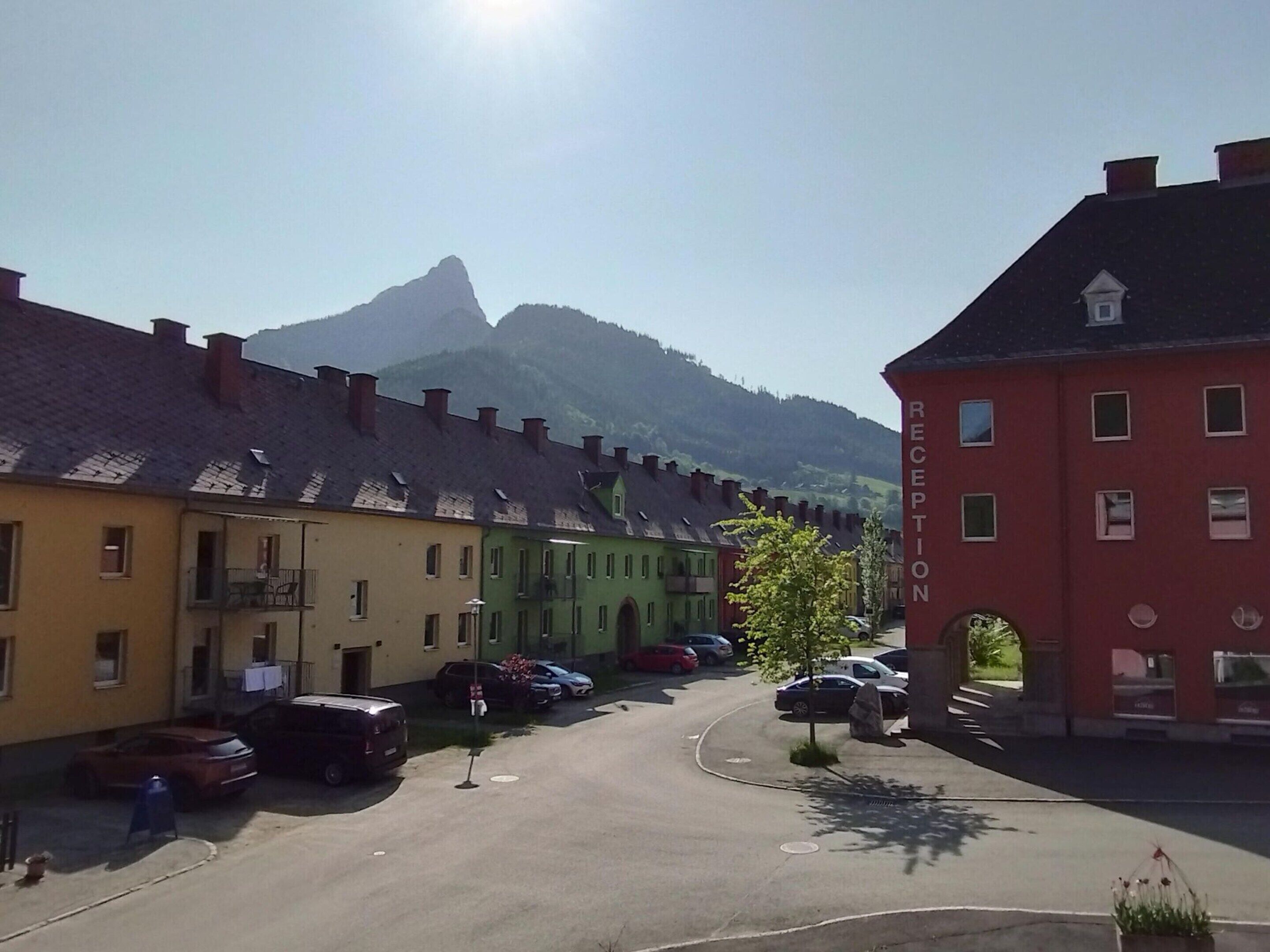 Une rue bordée d’immeubles aux couleurs vives, avec des voitures garées et une montagne en arrière-plan.