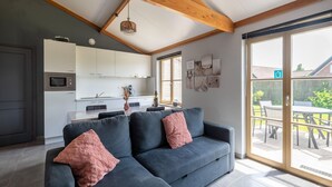 A modern kitchen with white cabinets, a built-in microwave, and a dining area with a table and chairs. - Holiday Home in Koksijde With Private Garden (Koksijde)