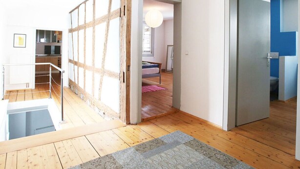 A spacious room with a wooden floor, a large window, and a view of a blue wall. - Holiday Apartment Faller-greiner (Bad Bergzabern)